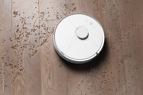 Smart robot vacuum cleaner removes scattered debris from the laminate floor, top view.