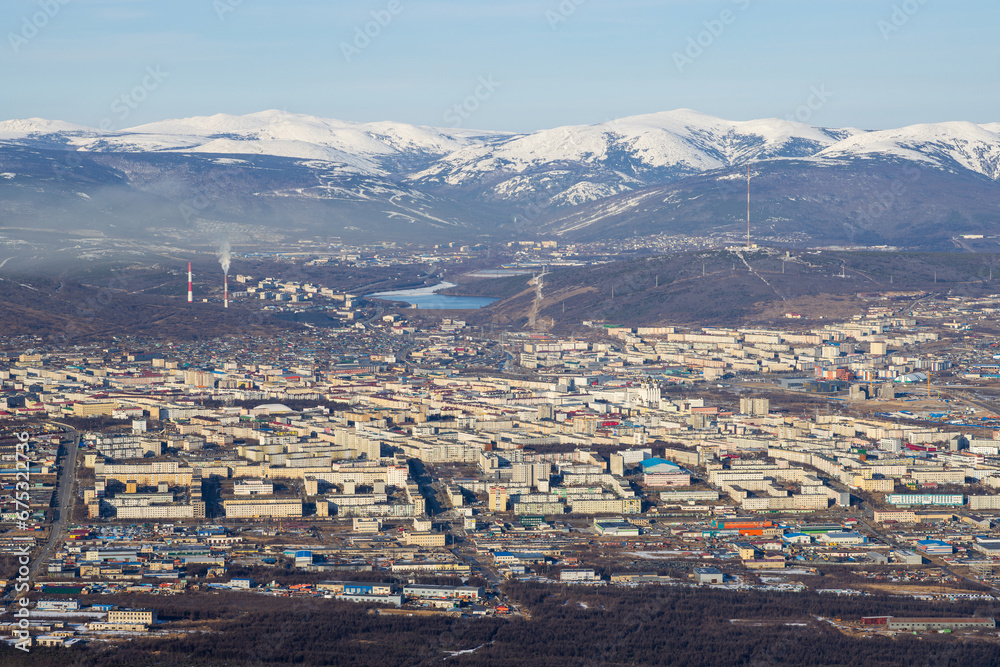 Top view of the city of Magadan. A large northern city in a valley among the mountains. Many buildings. Snow-capped mountains in the distance. Magadan, Magadan region, Russian Far East.