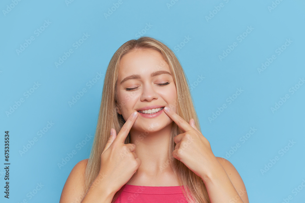 Beautiful girl with long white hair smiling with closed eyes against blue background, touching the corners of her mouth, beauty concept, copy space Beautiful girl with long white hair smiling with closed eyes against blue background, touching the corners of her mouth, beauty concept, copy space