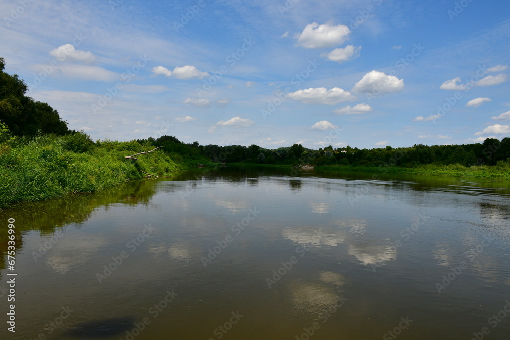 View of a massive lake, river, or pond surrounded from all sides with reeds, moss, forests, moors, and other flora spotted on a cloudy yet warm summer day next to some holiday resort located in Poland View of a massive lake, river, or pond surrounded from all sides with reeds, moss, forests, moors, and other flora spotted on a cloudy yet warm summer day next to some holiday resort located in Poland