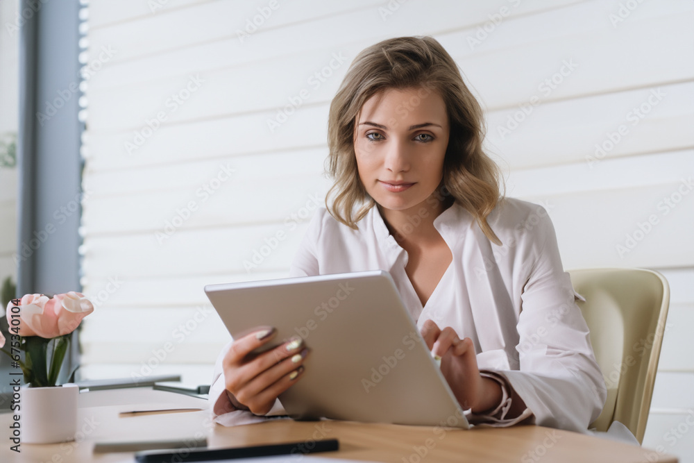 girl works in the office. blonde woman doing work on a tablet in her office, white wall in the background. business business work in an office building concept girl works in the office. blonde woman doing work on a tablet in her office, white wall in the background. business business work in an office building concept