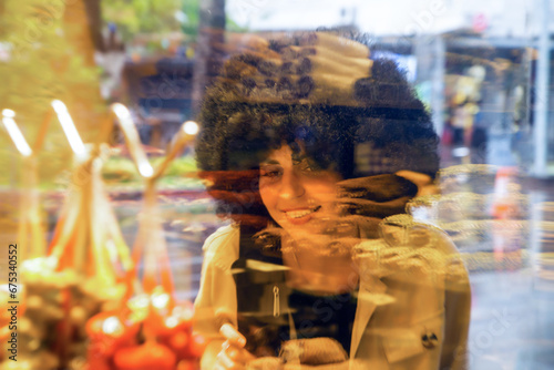 A woman with black curly hair looks store window with sweets, pastries and cakes.