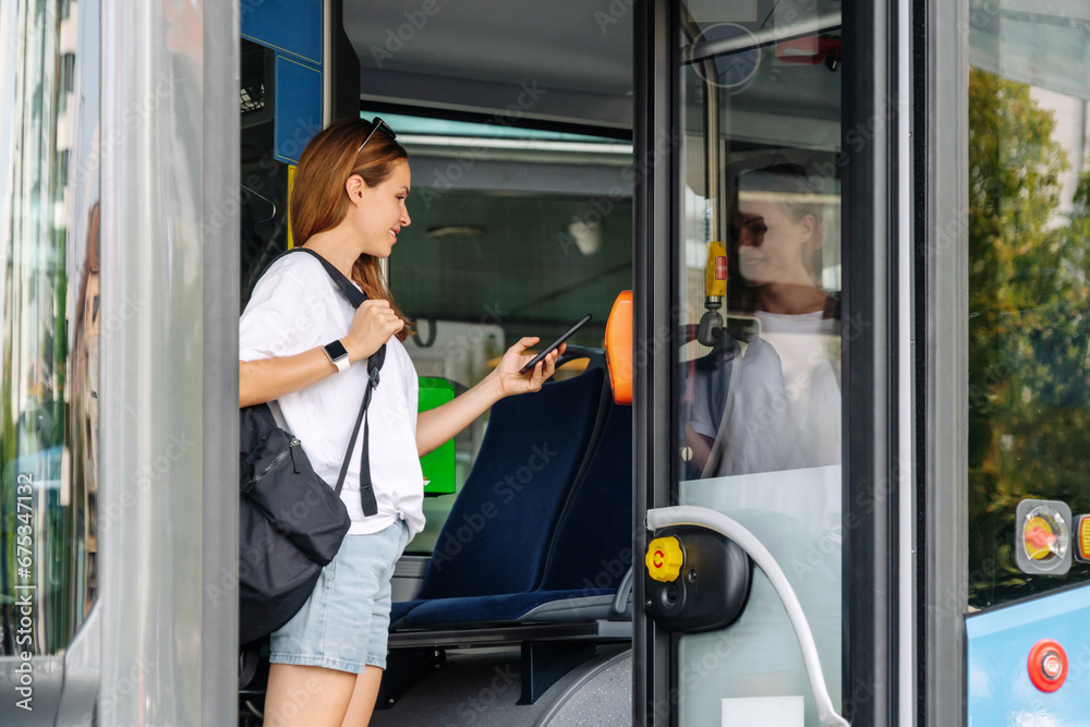 Urban woman passenger of public transportation pays bus with her mobile phone and contactless payment technology. Urban woman passenger of public transportation pays bus with her mobile phone and contactless payment technology.