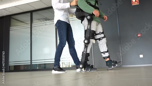 Mechanical exoskeleton, physiotherapist walking with unrecognizable disabled person with robotic skeleton, physiotherapy in a modern hospital: photo