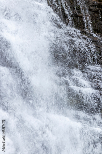 close-up photo of a frothy, white waterfall cascading down a dark, jagged cliff face, ai generative