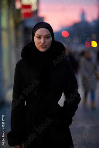 Muslim woman walking on an urban city street on a cold winter night wearing hijab