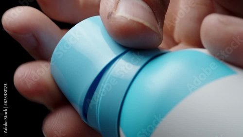 A man's hand removes the blue cap from the deodorant bottle, close-up. photo