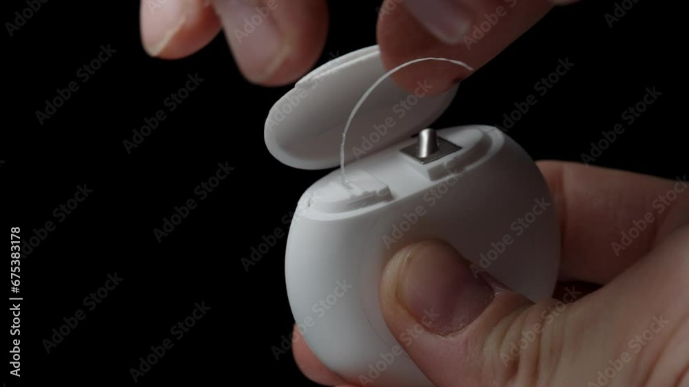 A White Dental Floss Container, a man pulls out a length of floss and cuts it using the designated area on the packaging. A White Dental Floss Container, a man pulls out a length of floss and cuts it using the designated area on the packaging.