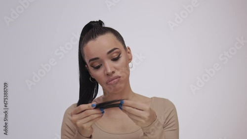 A beautiful brunette examines the ends of her hair. Damaged hair and unhappy face photo