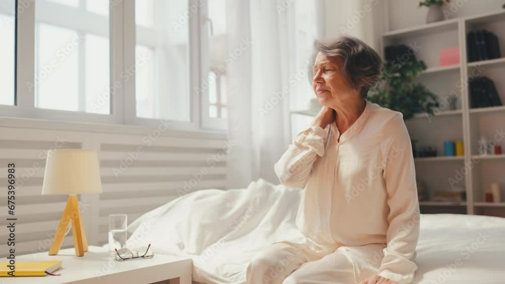 Senior woman suffering from neck pain while sitting on bed, muscle inflammation Senior woman suffering from neck pain while sitting on bed, muscle inflammation