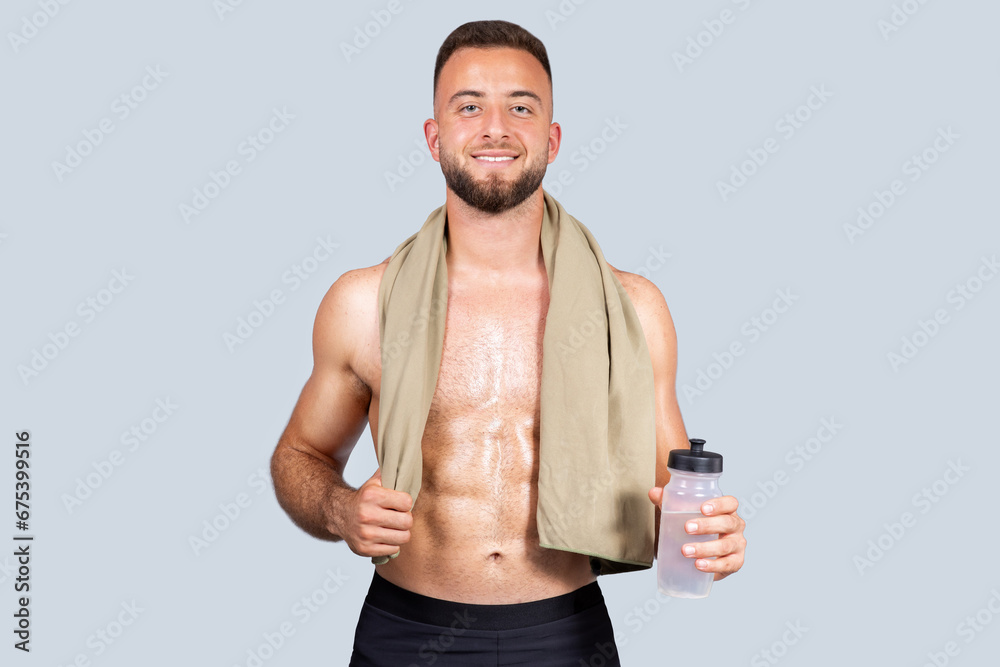 Cheerful sweat strong muscular young european man with beard, naked torso, towel, hold bottle of water Cheerful sweat strong muscular young european man with beard, naked torso, towel, hold bottle of water