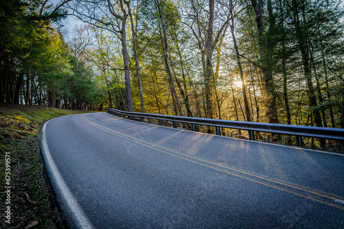 Winding uphill road in the woods with sunset peeking through the trees in early spring time