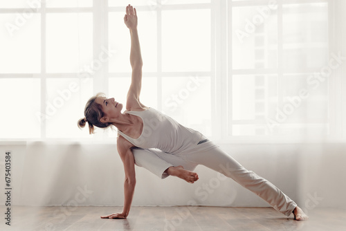 Fototapeta Naklejka Na Ścianę i Meble -  Portrait of beautiful fit young woman wearing white sporty outfit and doing yoga exercise, Beautiful and fit young woman in white athletic attire performing yoga poses.