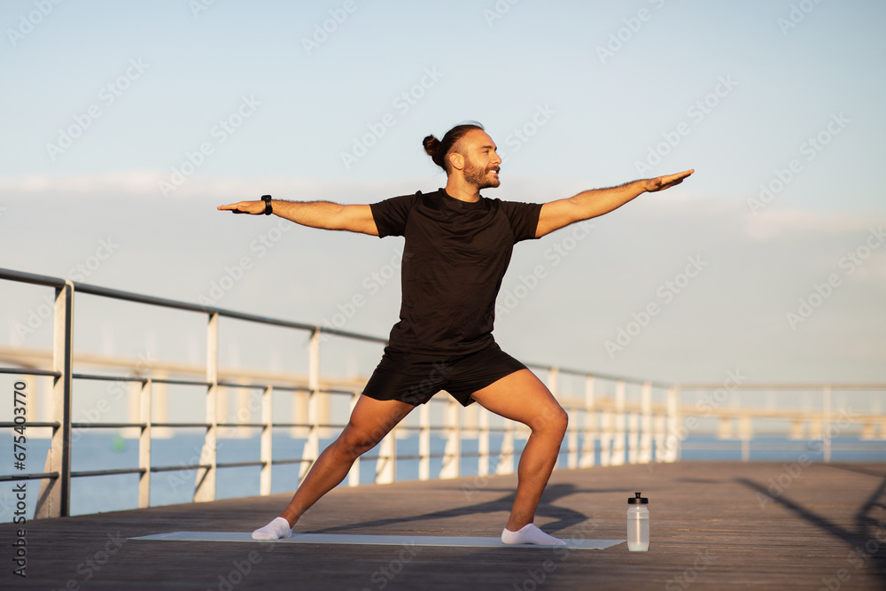 Sporty man striking yoga asana standing in warrior pose outside Sporty man striking yoga asana standing in warrior pose outside