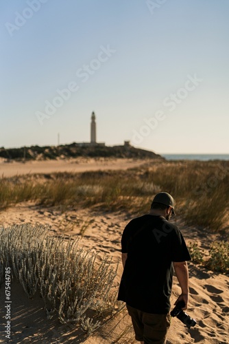 Male photographer walking along the shoreline of a beach.