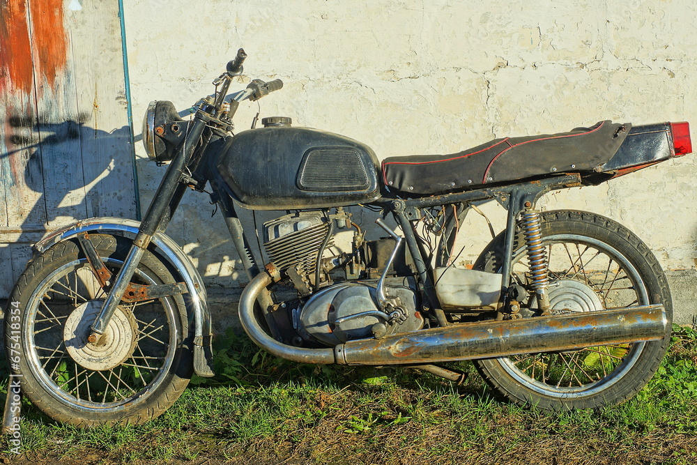 one old  iron classical  heavy big comfortable black  broken    dirty made in the ussr retro  motorcycle stands  near the white wall  on the ground in the street 
