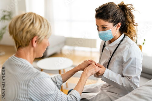 Senior woman consulting with female doctor while holding hands during home visit.