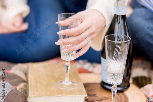 A woman is having a picnic on a rustic blanket, and she holds a glass with champagne, showing off her engagement ring