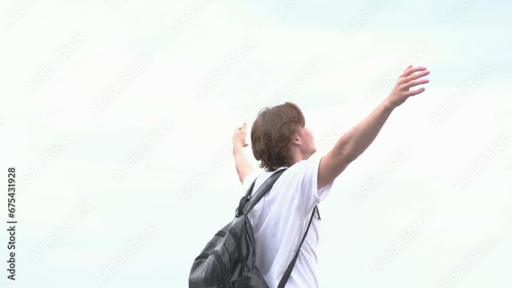 a cute young man with black backpack is raising hands to the sky, looking at sky and moving around. Consept of freedom. a cute young man with black backpack is raising hands to the sky, looking at sky and moving around. Consept of freedom.