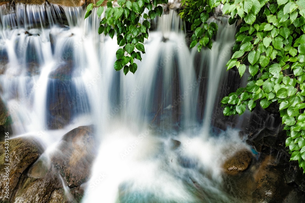 Long exposure shot of a cascading waterfall with a creek meanders through a lush forest - obrazy, fototapety, plakaty 