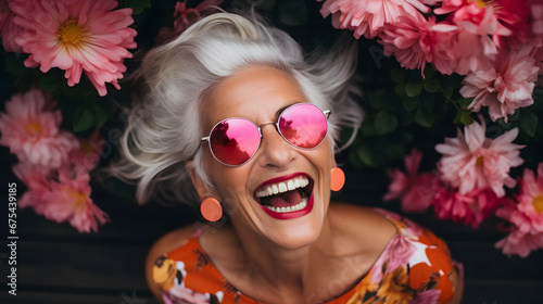 Beautiful senior woman with pink sunglasses and flowers on a wooden background. Fashion concept.