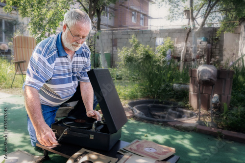 An elderly man in the garden starts up an old phonograph. A man is resting in the garden in nature.