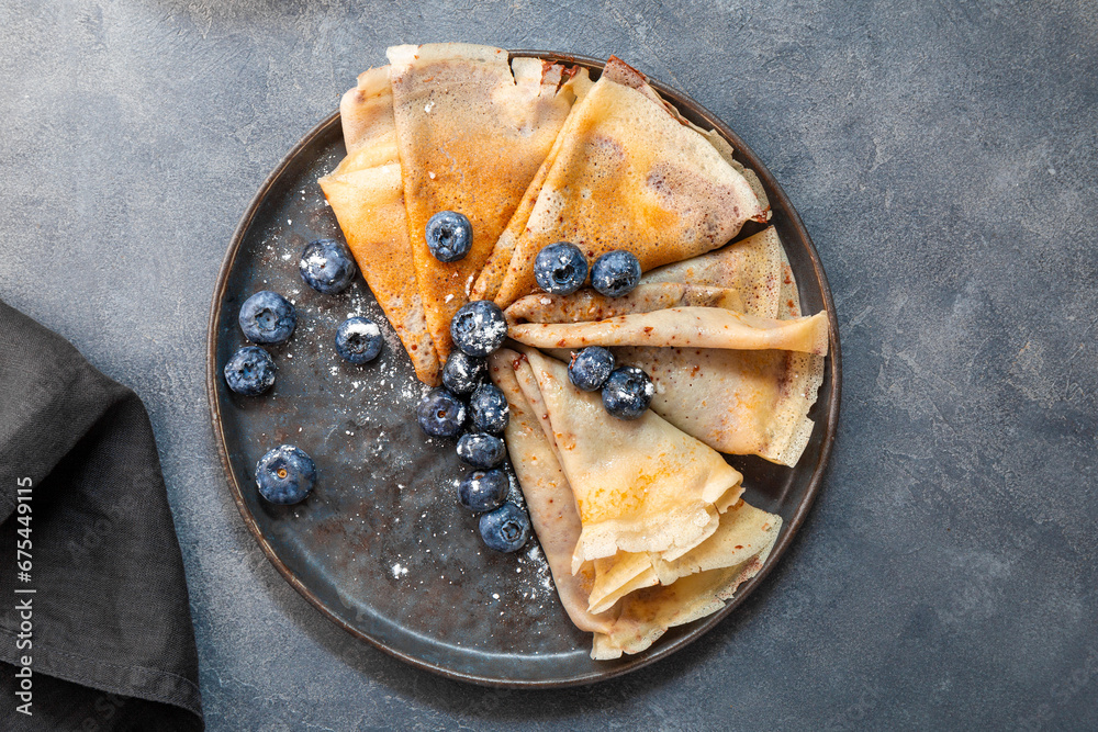 Thin pancakes with chocolate spread and blueberries on the grey background top view Thin pancakes with chocolate spread and blueberries on the grey background top view