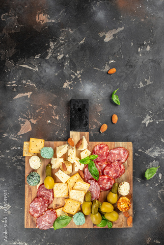 Cutting board with salami, cheese, bread and olives on dark stone background. vertical image. top view. copy space for text photo