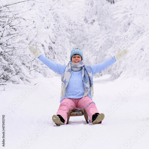 lachende Frau auf einem Schlitten im Winterwald