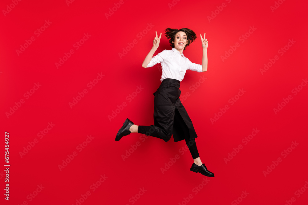 Full body profile side photo of charming happy nice young woman show v-sign jump up isolated on red color background Full body profile side photo of charming happy nice young woman show v-sign jump up isolated on red color background