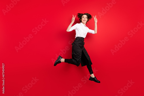 Full body profile side photo of charming happy nice young woman show v-sign jump up isolated on red color background