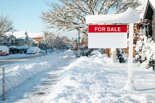 Home for sale sign with winter background scene on a sunny day. Red for sale realtor signage on sign post defocused snowed cars, homes and  street. Real estate and working in winter. Selective focus. photo