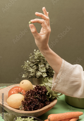 A woman's hand holding a pea in front of a green background