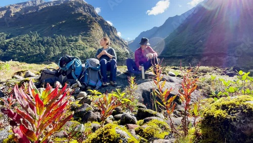 4K footage of Young Couple sitting on stones, resting, drinking tea in Makalu Barun National Park on Mera peak climbing route. They left Backpacks and trekking poles and enjoying valley sunny day view photo
