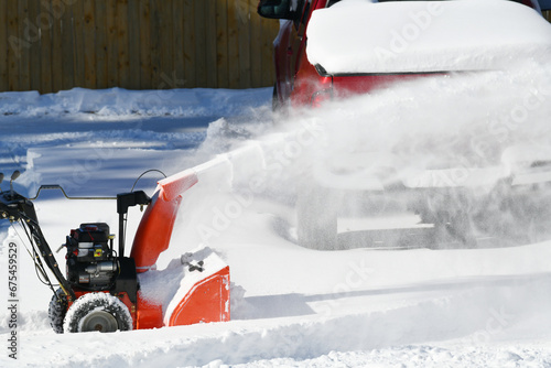 man removing snow on the driveway of the house by snow blower photo