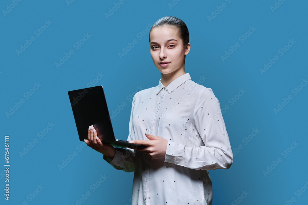 Serious teenage high school student girl using laptop on blue background Serious teenage high school student girl using laptop on blue background