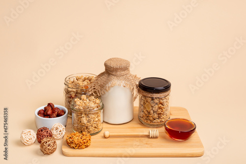 Healthy breakfast cereal. Granola with milk, glass of milk, honey, nuts and muesli cookie on light beige background.