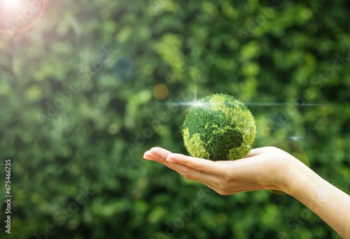 Hand holding a green grass earth globe with light reflection, flare light on natural background for global development.Friendly globe day, environmental management, energy or business concept.Banner.