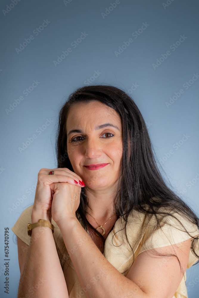 a woman with long brown hair and a white top holds her hands to her chin a woman with long brown hair and a white top holds her hands to her chin