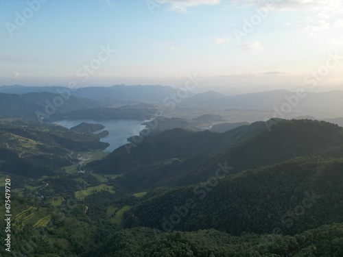 Misty aerial view of lush green rolling hills, with a blue lake and white fluffy clouds in the sky