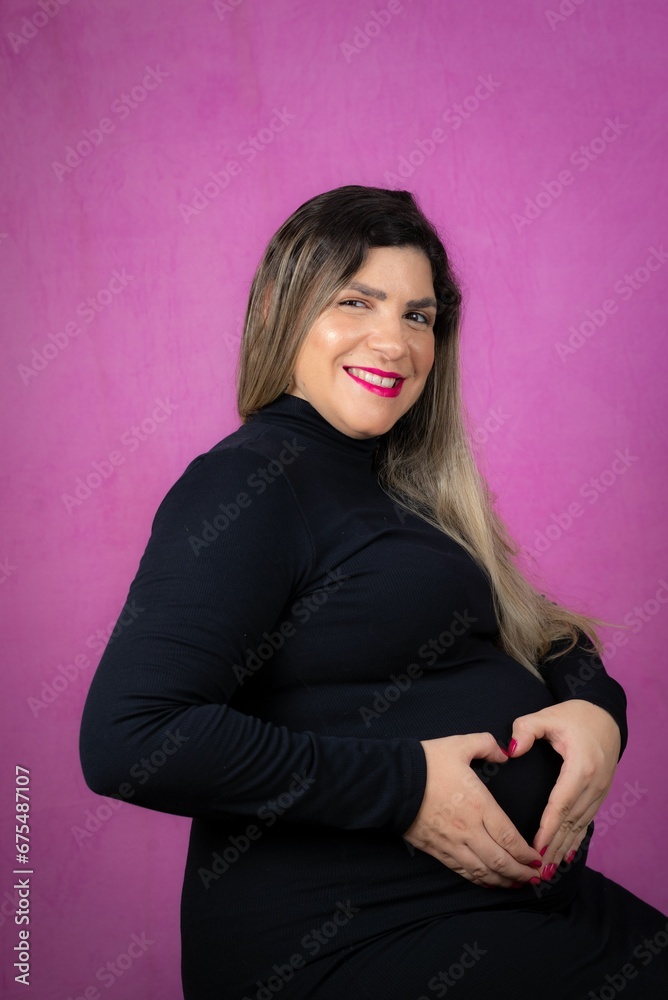 Fototapeta premium Smiling pregnant woman making a heart shape with both hands