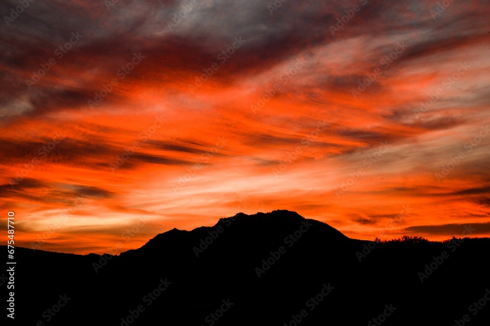 Sunset in red and orange hues over the silhouette of Granite mountain in Prescott, AZ.