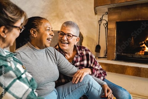 Multiracial senior friends by wood fireplace having fun together at rural home. Winter and fall season life style concept