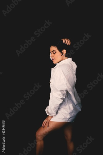 Young woman with an artistic expression wearing a white outfit poses on a black background