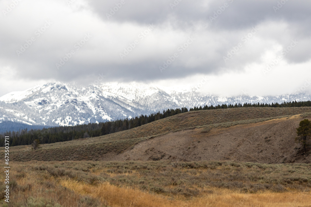 snow covered mountains in yellowstone, image shows a landscape image of the countryside, including forests at the base of the mountain and the snow covered mountain with dark clouds taken october 2023