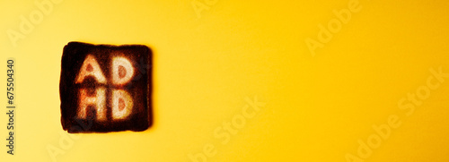 slice of dark burnt charred white bread with word ADHD on it on yellow background. Conceptual image absent-minded cooking. 
 unfocused, lack of concentration. long horizontal banner photo