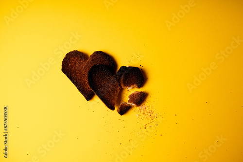 Broken hearted. Two burnt hearts made of white toast bread on yellow background. Conceptual romantic traumatic relationship idea photo