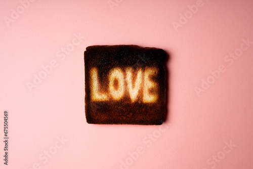 Love symbol on burnt dark slice of white bread toast with the word Love on it. creative concept composition representation passionate feeling. Pink background poster