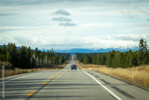 road to the mountains, image shows a endless road heading towards the mountains with a few vehicles on the road and a mountain range in the distant, with grey clouds above, taken october 2023