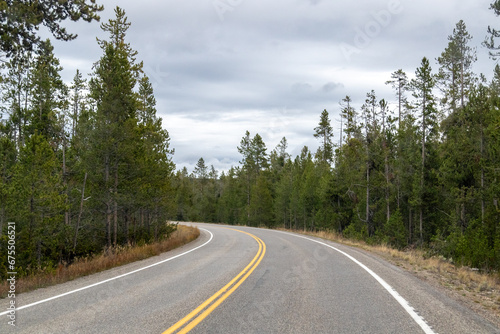 road to the mountains, image shows a bending road heading towards the yellowstone mountains no on the road and a view of the forest either side, with grey clouds above, taken october 2023